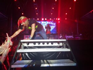 Bret Michaels on his hands and knees in the pouring rain, reaching out to touch fans during a live performance.