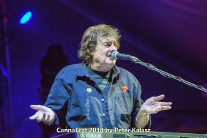 Burton Cummings sitting at a keyboard, speaking to the crowd during a live performance.