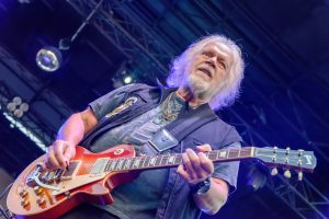 Randy Bachman playing guitar on stage, looking at the crowd during a live performance.