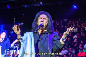 Gene Simmons talking to the crowd while holding his sunglasses during a live performance.